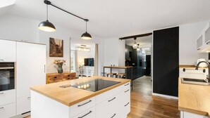 Cocina moderna con armarios blancos, encimera de madera e iluminación colgante.