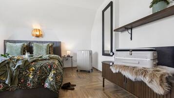 A bedroom with a bed, bedside table, lamp, suitcase, and a mirror on the wall.