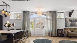 Un área de comedor con una mesa y sillas, un sofá y un amplio ventanal con cortinas.