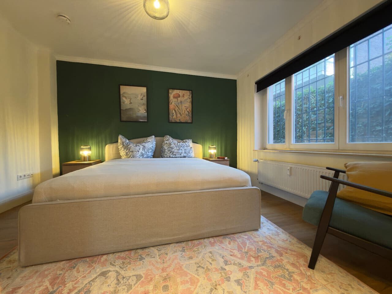 Une chambre à coucher avec un grand lit, deux lampes de chevet, une fenêtre donnant sur un beau paysage et un radiateur.