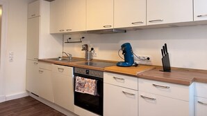 Une cuisine moderne avec des meubles blancs, un four encastré, une machine à café et un bloc à couteaux.