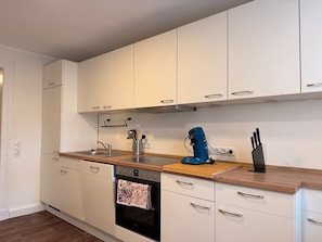 A modern kitchen with white cabinets, a built-in oven, a coffee machine, and a knife block.