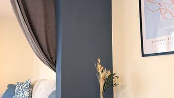 Ein modernes Zimmer mit einer dunkelblauen Akzentwand, einem blauen Beistelltisch mit einer Vase, einem gerahmten Bild und einem Sofa mit gemusterten Kissen.