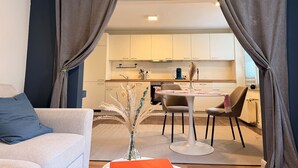 Un salon moderne avec un canapé, une table à manger et des chaises, et un coin cuisine visible à travers une porte.