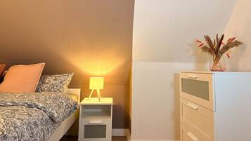 Et soveværelse med en seng, et natbord med lampe, en kommode og en vase med tørrede planter.