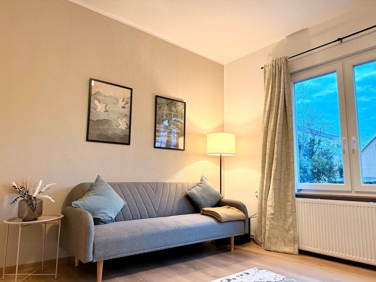 A living room with a sofa, a lamp, and a window with curtains.