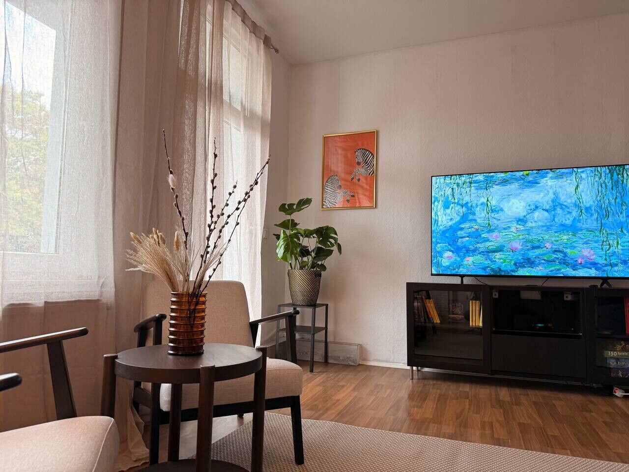 Ett vardagsrum med en tv, en växt och en vas på ett bord.
