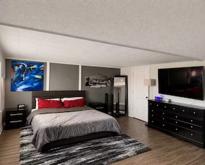 A modern bedroom with a bed, a TV, a dresser, and a painting on the wall. - Cozy Family House 5 mins From Chiefs & Royals Stadium (Raytown)