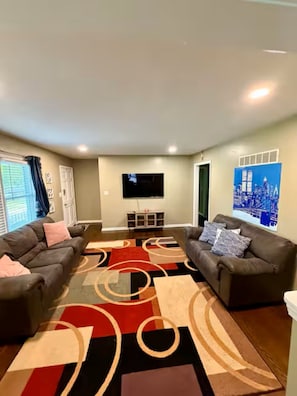 A living room with two sofas, a flat-screen TV, and a cityscape painting. - Cozy Family House 5 mins From Chiefs & Royals Stadium (Raytown)