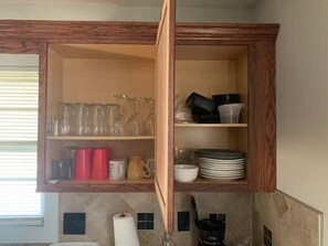 A kitchen with a wooden cabinet containing glassware, cups, and plates. - Cozy Family House 5 mins From Chiefs & Royals Stadium (Raytown)