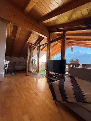 Ein Holzinnenraum mit Fernseher, Sofa und Blick auf Berge.