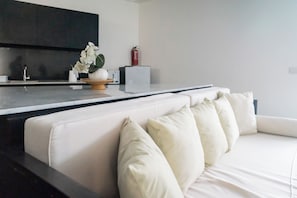 A modern living room with a white sofa, a kitchen area with dark cabinets, and a small plant on the counter. - Serenity Villa Nusa Dua (Badung)