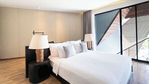 A modern hotel room with a large bed, two bedside tables with lamps, a view of a staircase, and a large window. - Serenity Villa Nusa Dua (Badung)