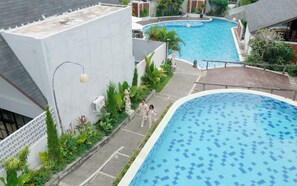A swimming pool with a tiled pattern, surrounded by greenery and a white building with a sloped roof. - Serenity Villa Nusa Dua (Badung)