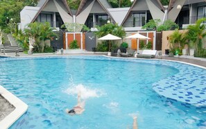 A swimming pool with a person swimming, surrounded by modern buildings and outdoor seating. - Serenity Villa Nusa Dua (Badung)