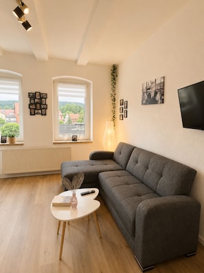 En moderne stue med en modulsofa, et rundt sofabord, en gulvlampe og et fladskærms-tv monteret på væggen.