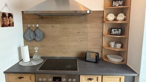 Une petite cuisine équipée avec une cuisinière, un four et un grille-pain. On y trouve des placards en bois et une étagère avec des ustensiles de cuisine.