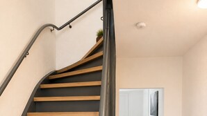 Un escalier avec des marches en bois et une rampe sombre, menant à une porte à côté de laquelle se trouve une plante.