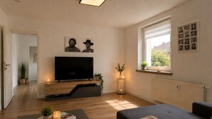 Ein Wohnzimmer mit Fernseher, Sofa und einem kleinen Tisch mit Fernbedienung und Kerze.