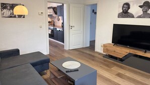 Ein modernes Wohnzimmer mit Sofa, Couchtisch, Fernseher und einer Küche im Hintergrund.