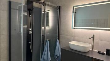 Ein modernes Badezimmer mit einer gläsernen Dusche, einem weißen Waschbecken und einem Spiegel darüber.