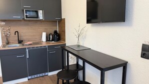 Una cocina compacta con microondas, cafetera y una pequeña mesa con taburetes.