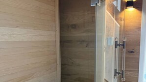 Un interior de madera con cabina de ducha de vidrio, un estuche de almacenamiento tipo piedra y suelo de madera.