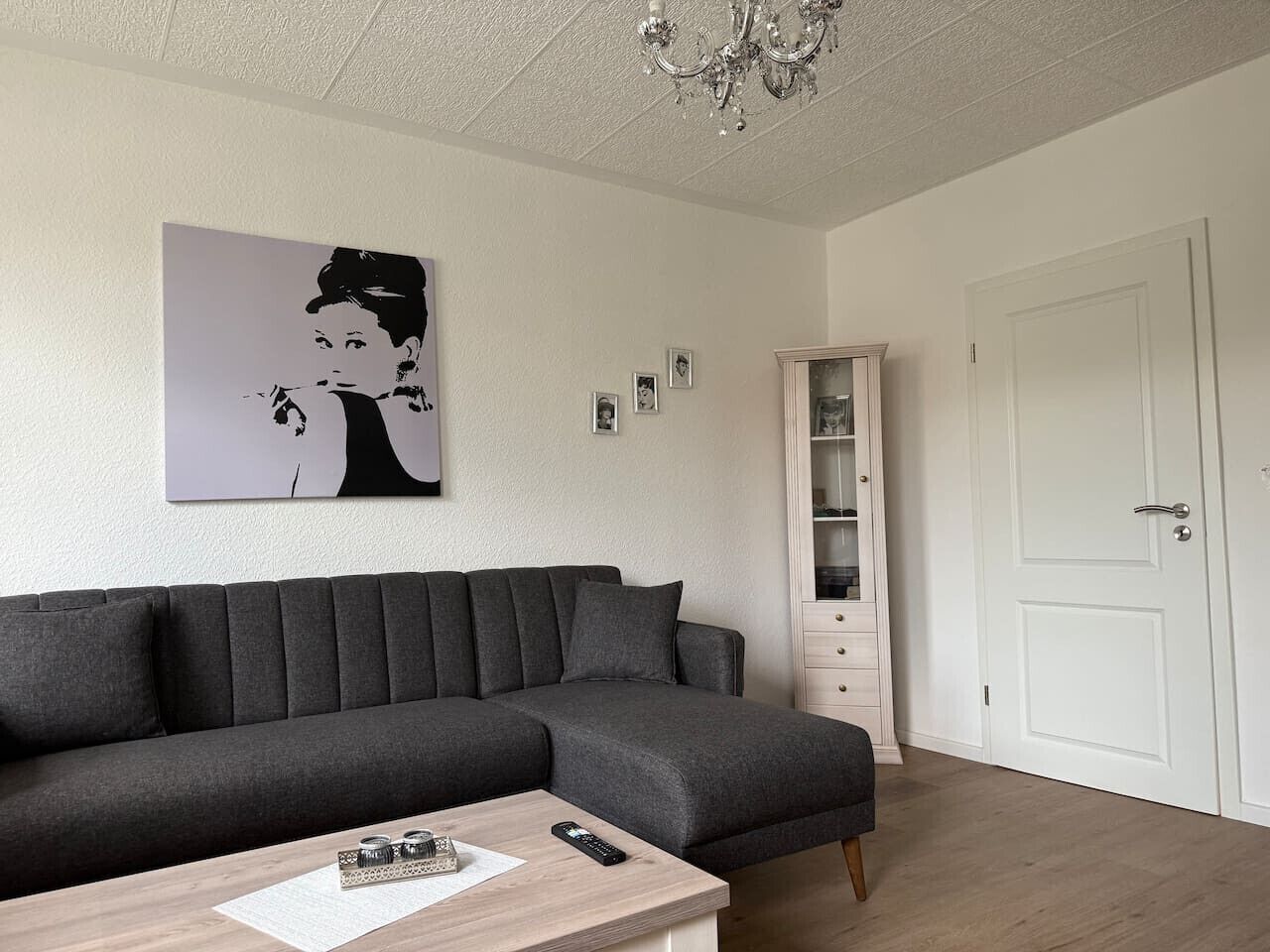 Ein modernes Wohnzimmer mit einem Ecksofa, einem Holztisch, einer Pendelleuchte, einer weißen Tür und einer eingebauten Regaleinheit.