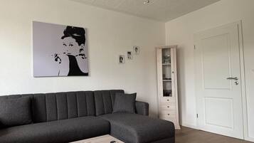 Ein modernes Wohnzimmer mit einem Ecksofa, einem Holztisch, einer Pendelleuchte, einer weißen Tür und einer eingebauten Regaleinheit.