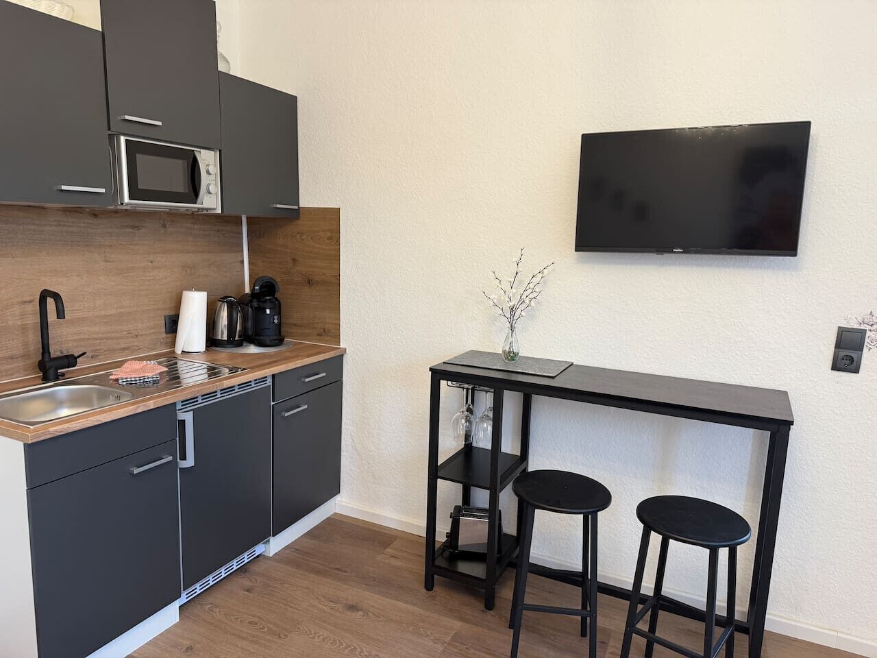 A compact kitchen with a microwave, coffee maker, and a small bar area with stools.