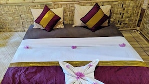 A bed with a white and purple bedspread, two pillows with a gold and purple design, and a decorative pillow with a floral pattern. - CJs Bungalow (Gili Trawangan)