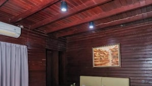 A wooden room with a bed, a painting on the wall, and a window with curtains. - CJs Bungalow (Gili Trawangan)