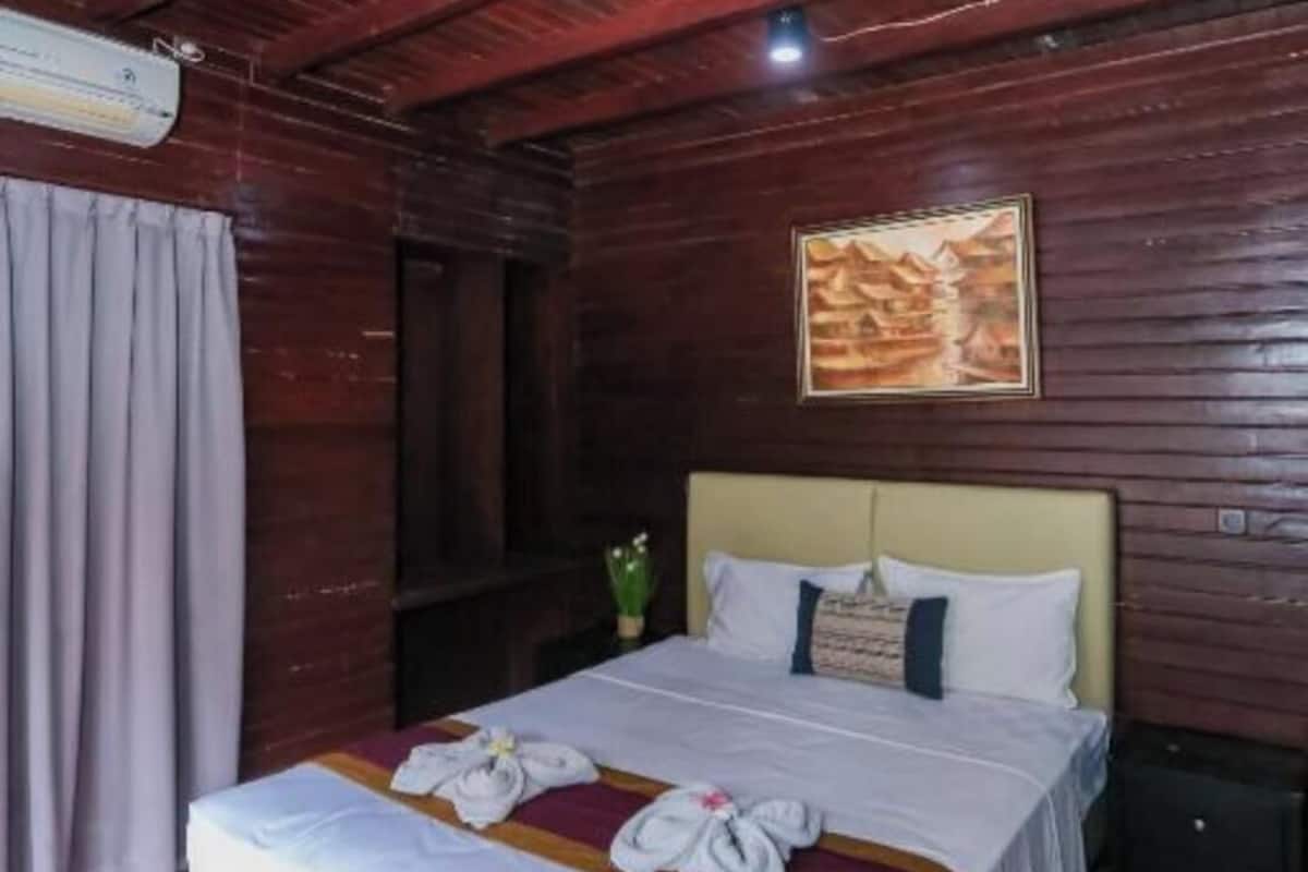 A wooden room with a bed, a painting on the wall, and a window with curtains.