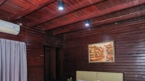 A wooden room with a bed, a painting on the wall, and a window with curtains. - CJs Bungalow (Gili Trawangan)