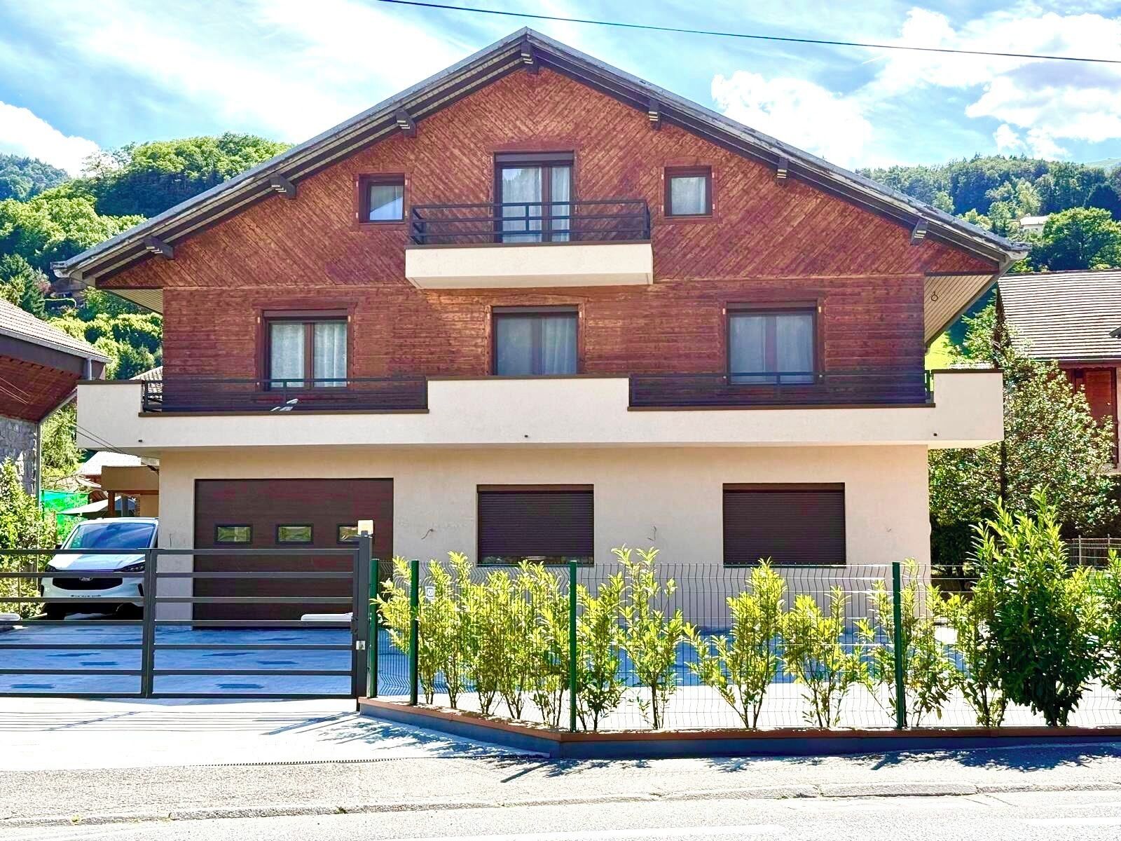 A two-story house with a wooden facade, a balcony on the upper floor, and a gated driveway.
