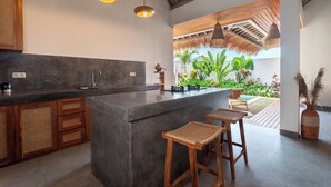 Une cuisine moderne dotée d’un îlot central, de tabourets de bar, de luminaires suspendus et offrant une vue sur un jardin tropical.
