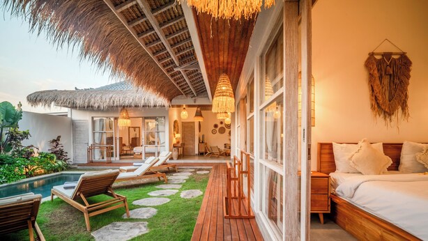 Une chambre avec un grand lit, une terrasse en bois et un espace piscine avec des chaises longues.