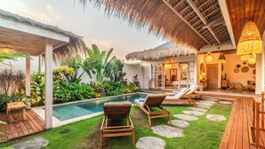 Un espace piscine doté de chaises longues, d’un toit de chaume et de plantes tropicales.