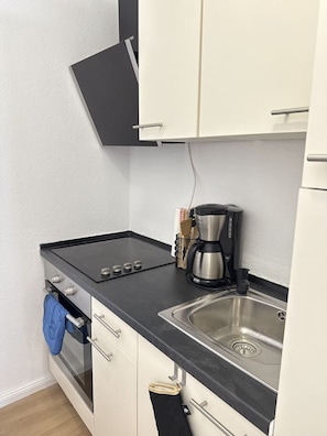 Een kleine keuken met een fornuis, spoelbak en koffiezetapparaat.