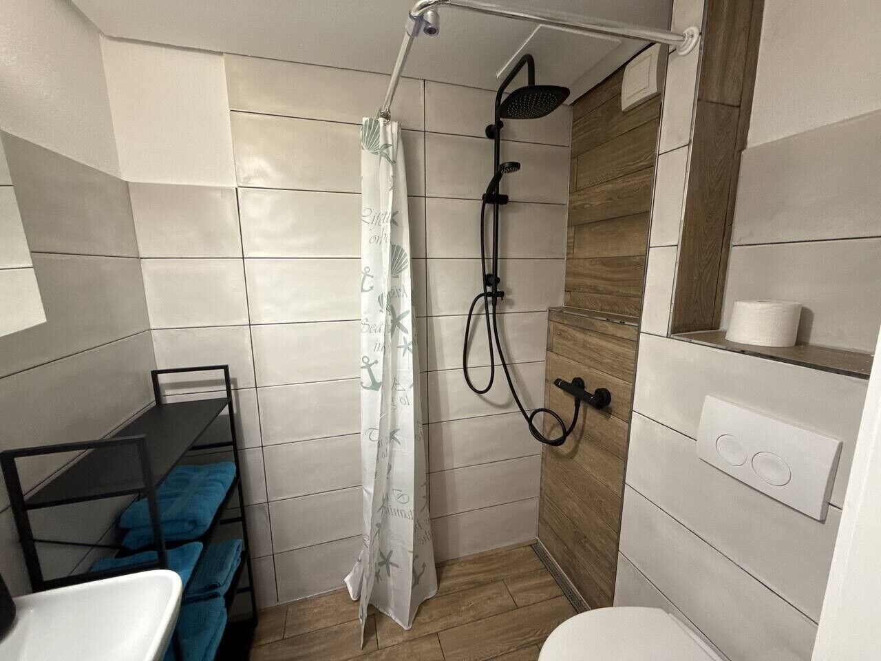 Une petite salle de bain comprenant une douche, un petit lavabo et une étagère avec des serviettes.