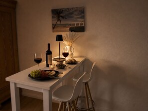 Ein Esstisch mit Stühlen, eine Weinflasche, ein Weinglas, eine Oliven-Schale, ein Teller mit Essen und eine dekorative Vase.