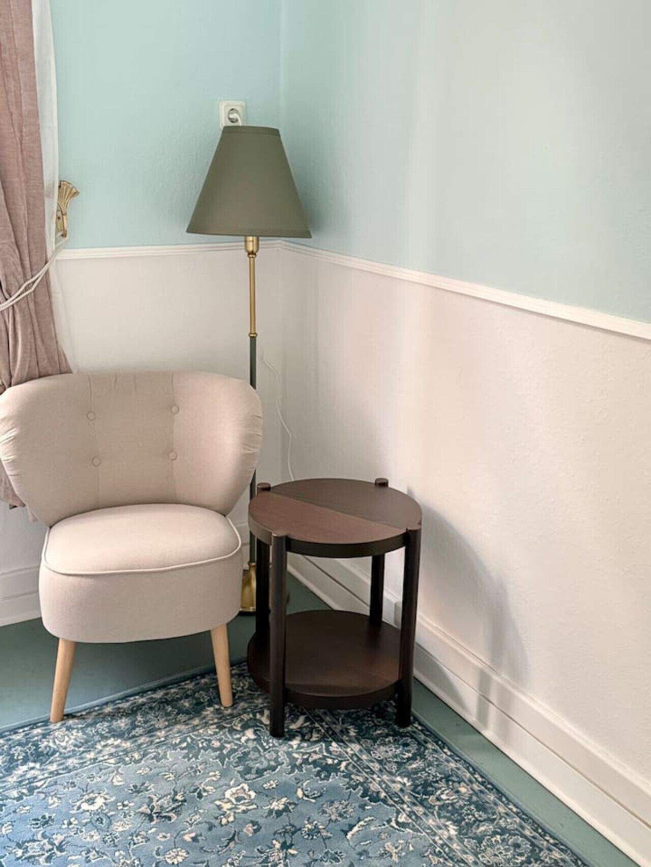 A corner room with a light blue wall, a beige armchair, a small round table, and a floor lamp.