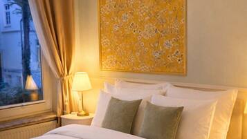 Une chambre d’hôtel avec un lit, une table de chevet, une lampe, une fenêtre avec des rideaux et une œuvre d’art florale accrochée au mur.