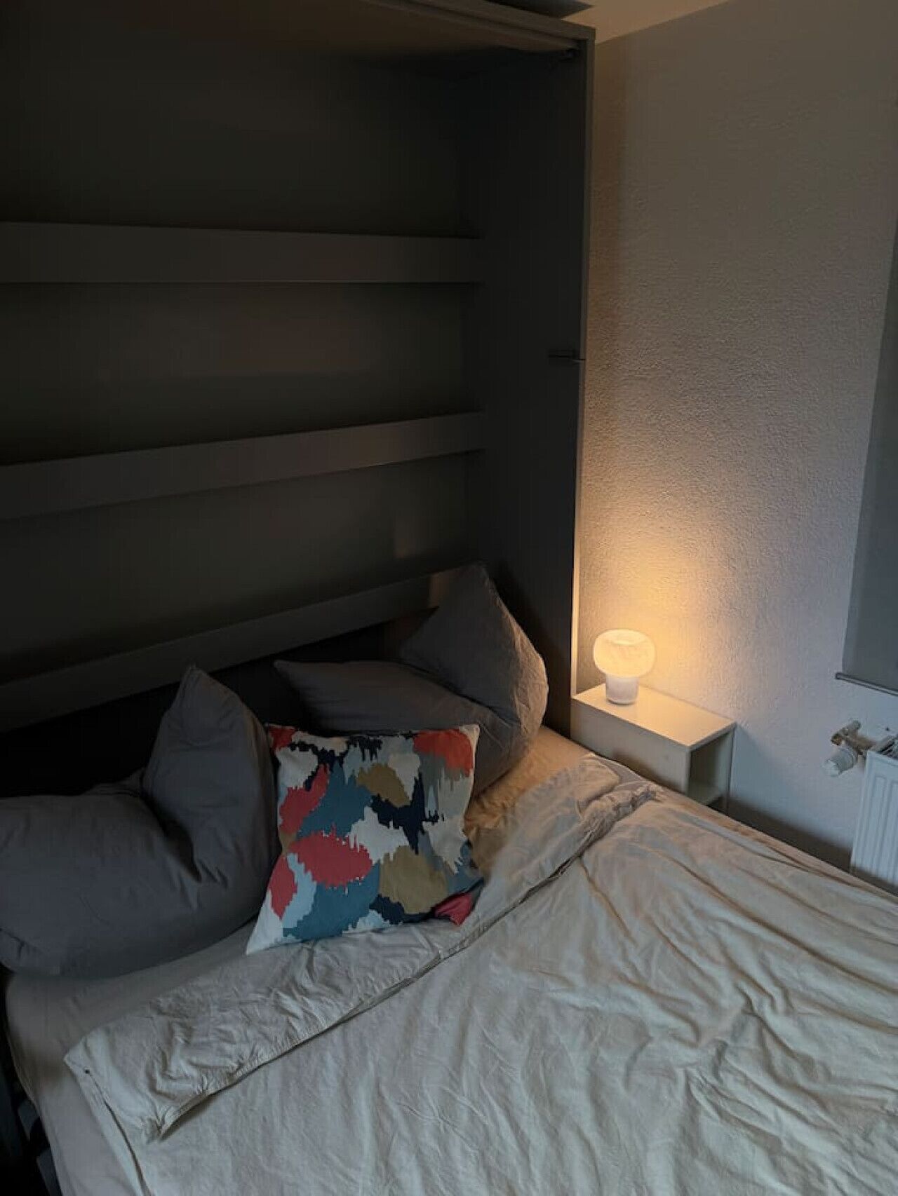 Ein Bett mit Kissen, eine Nachttischlampe und ein Heizkörper an der Wand.
