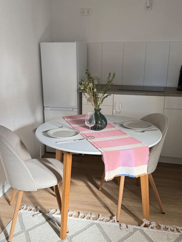 Ein Essbereich mit rundem Tisch, Stühlen, einer Vase mit Blumen und einer Küche im Hintergrund.