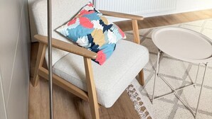 Una habitación con una silla, una lámpara, una ventana con persianas, un radiador y una mesita.