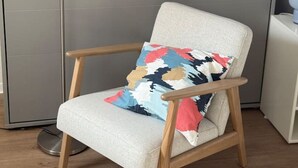Una silla con un cojín estampado, una lámpara de pie y una mesita auxiliar blanca.