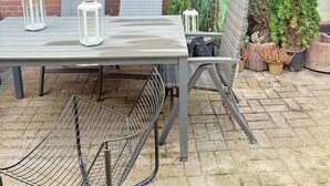 Un patio al aire libre con pared de ladrillo, una mesa con sillas, faroles y plantas en macetas.