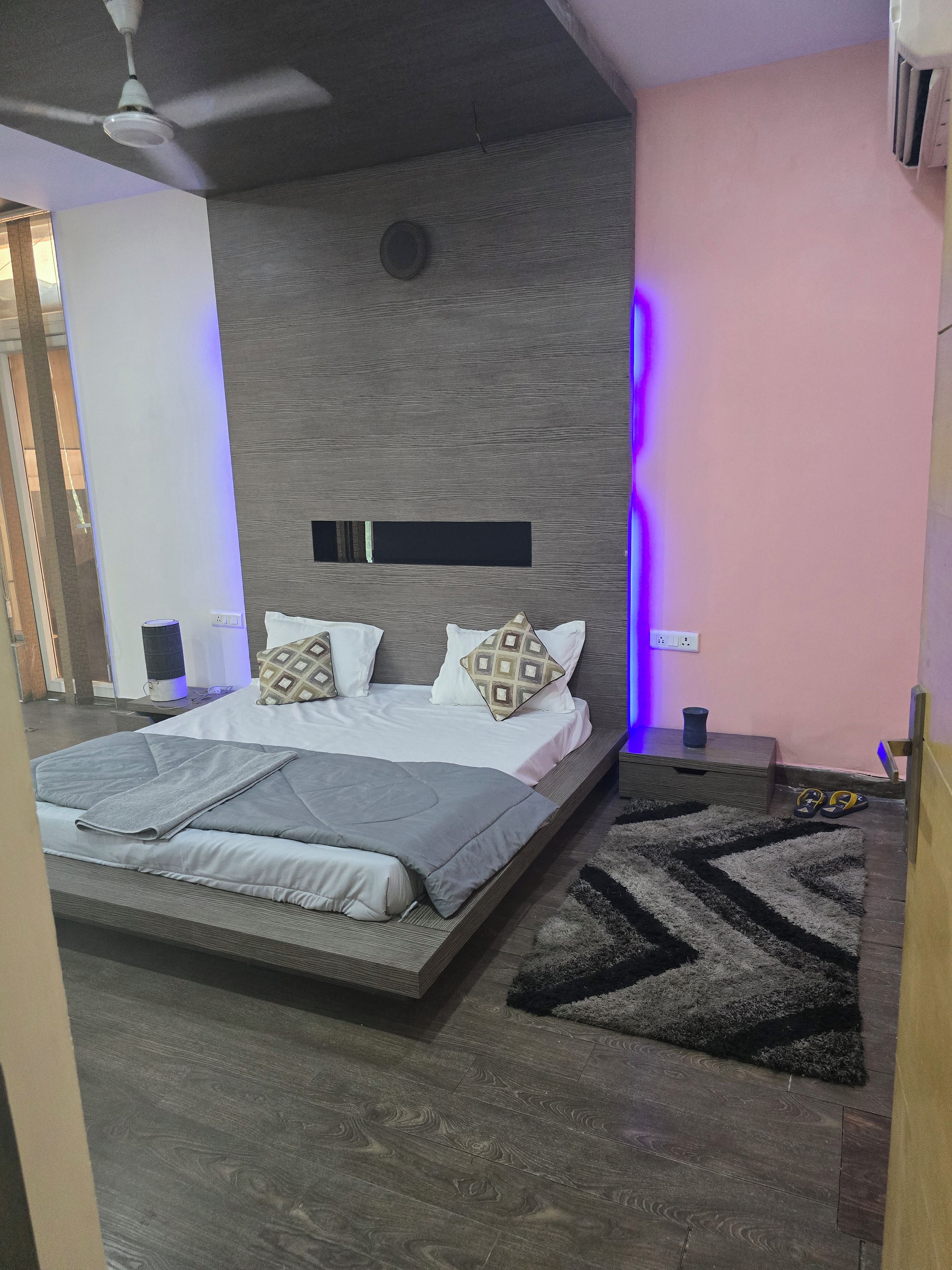 A modern bedroom with a bed, a ceiling fan, a nightstand, and a rug.