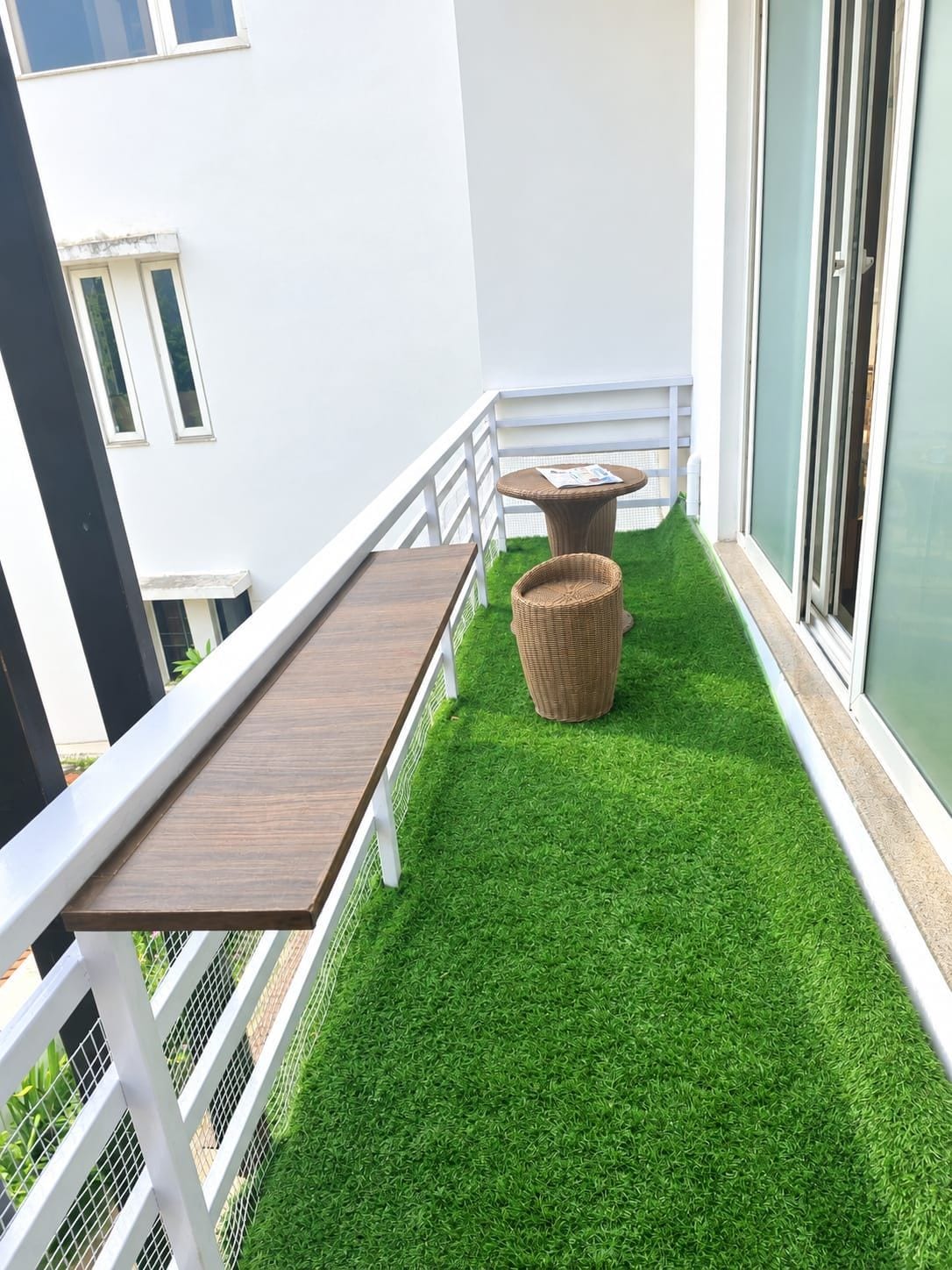 A balcony with artificial grass, a wooden table, and a wicker chair.